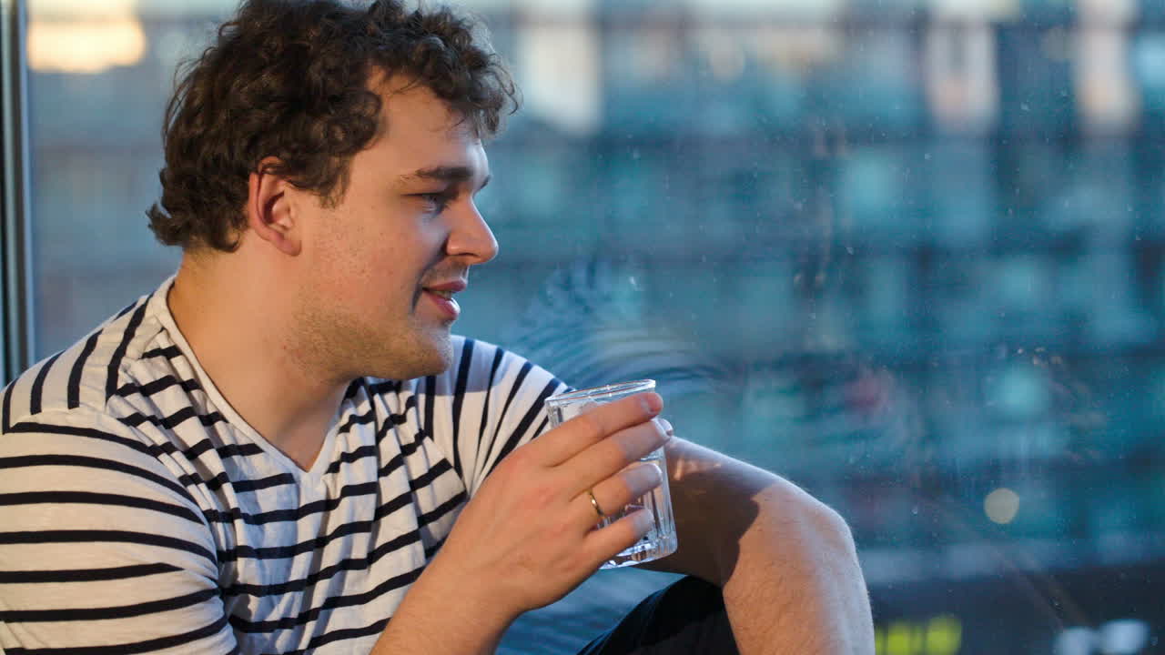 hombre feliz sentado junto a la ventana con un vaso de agua