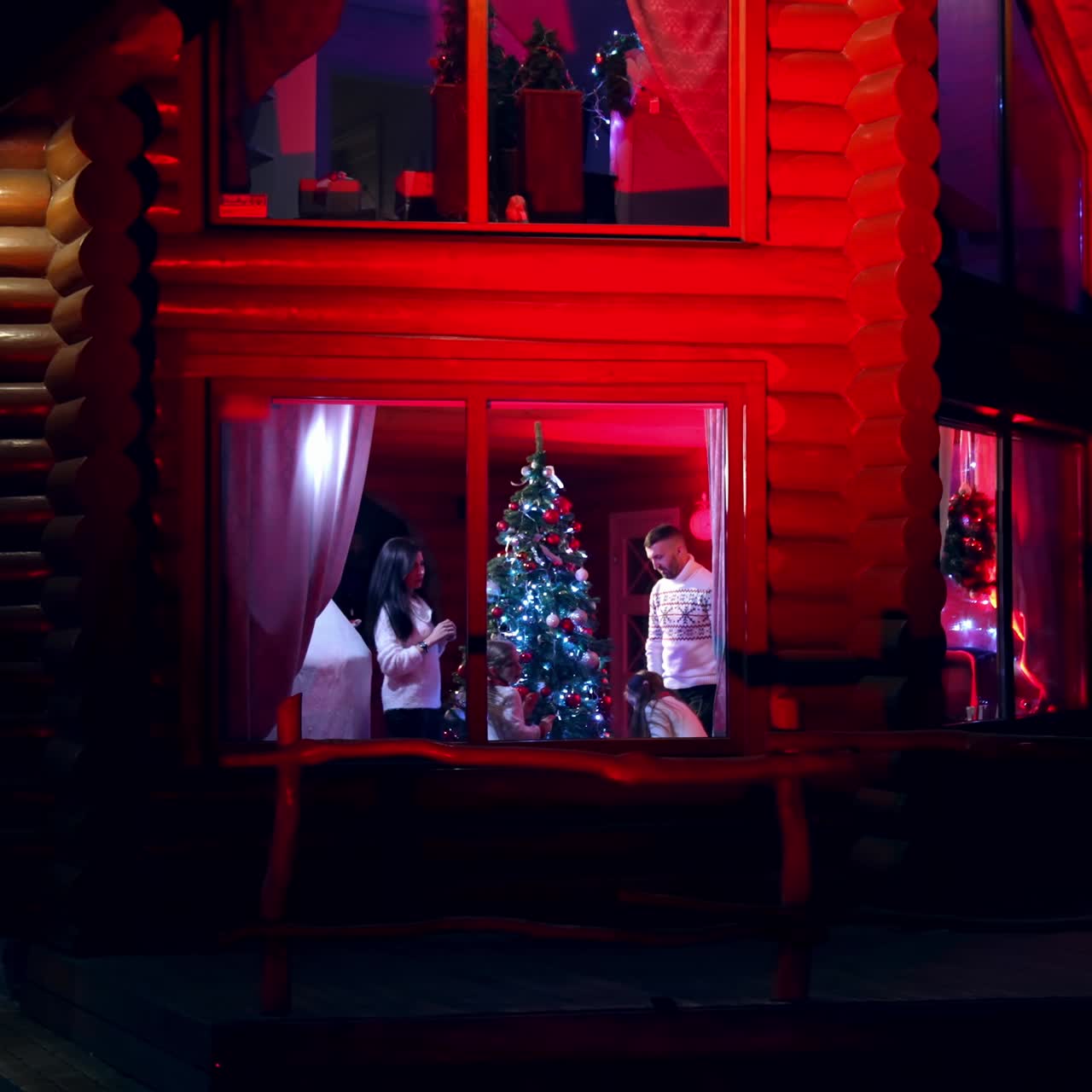 Family prepares for Christmas. Married couple with kids decorate New Year tree together. Festive mood at Christmas. View into the window of cozy house