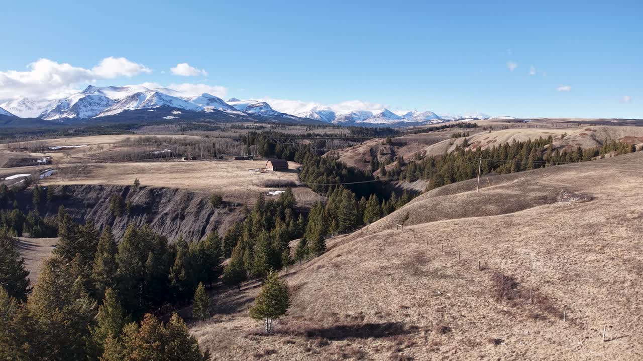 Drönarfilm fångar en torr gräsbevuxen dal med spridda träd och avlägsna snötäckta berg nära Whitefish, Montana.