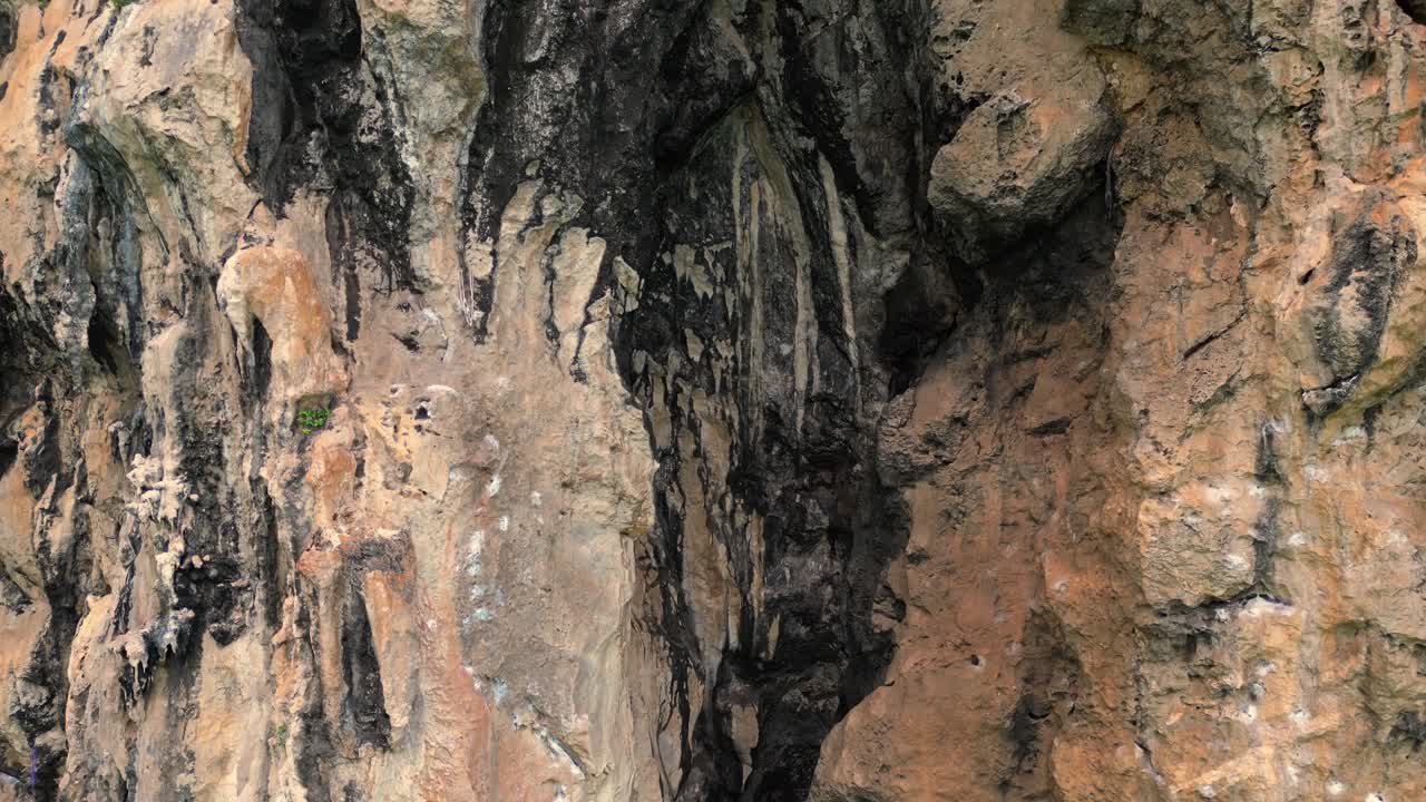 Rock climber resting during a difficult climb on Rai Leh beach cliff in Thailand. Smooth aerial view flight lift off raise up drone