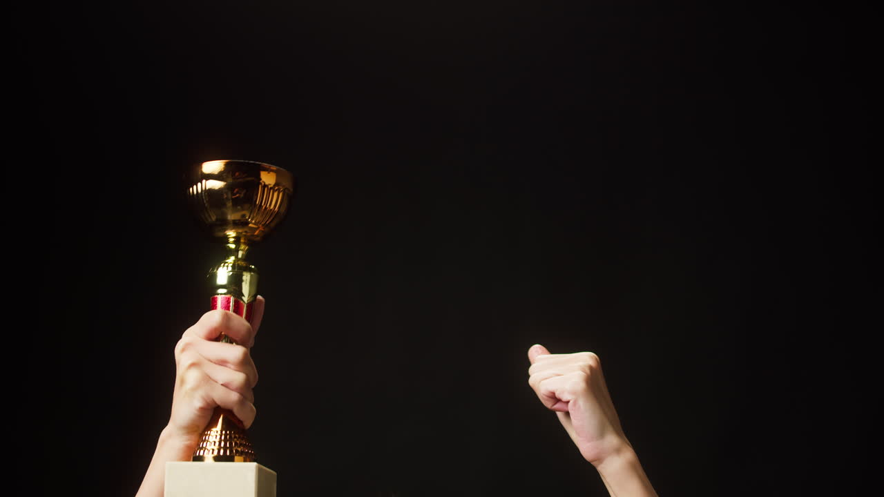 Hands Raising a Golden Trophy in Celebration on Black Background