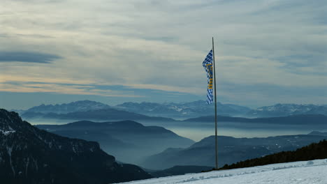 bavarian flag stands tall in a snow-covered mountainous region with a breathtaking horizon