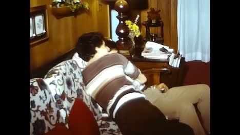man and woman sitting on couch in 1970s usa. circa usa - 1970s: a man and woman casually seated side by side on a couch in a typical 1970s american living room.