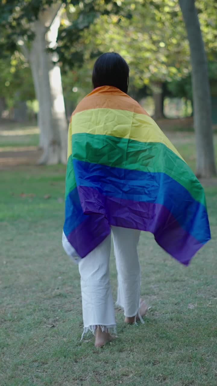 Person walking in a park with a rainbow flag