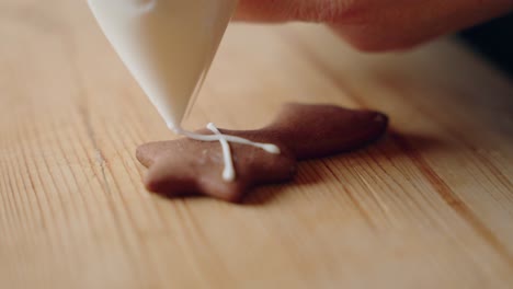 decorar galletas de pan de jengibre para navidad, macro toma de primer plano haciendo dulces y galletas de año nuevo hechos a mano con glaseado blanco