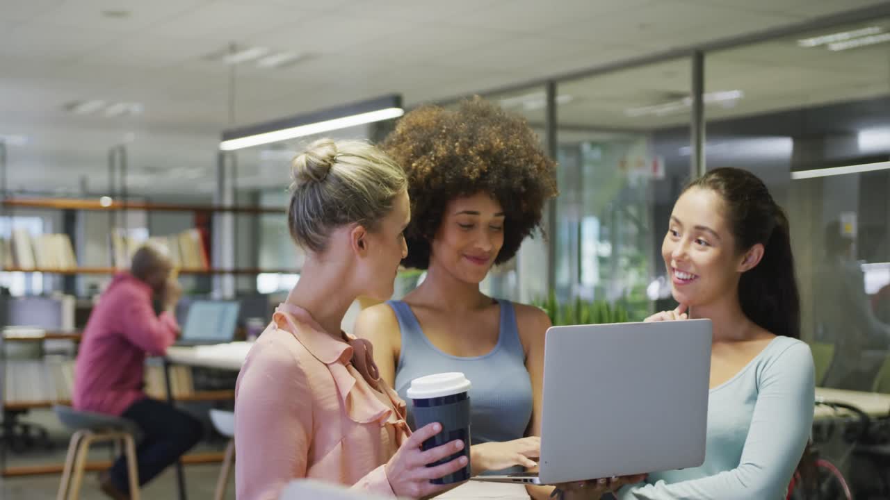 Diverse female business colleagues talking and using laptop