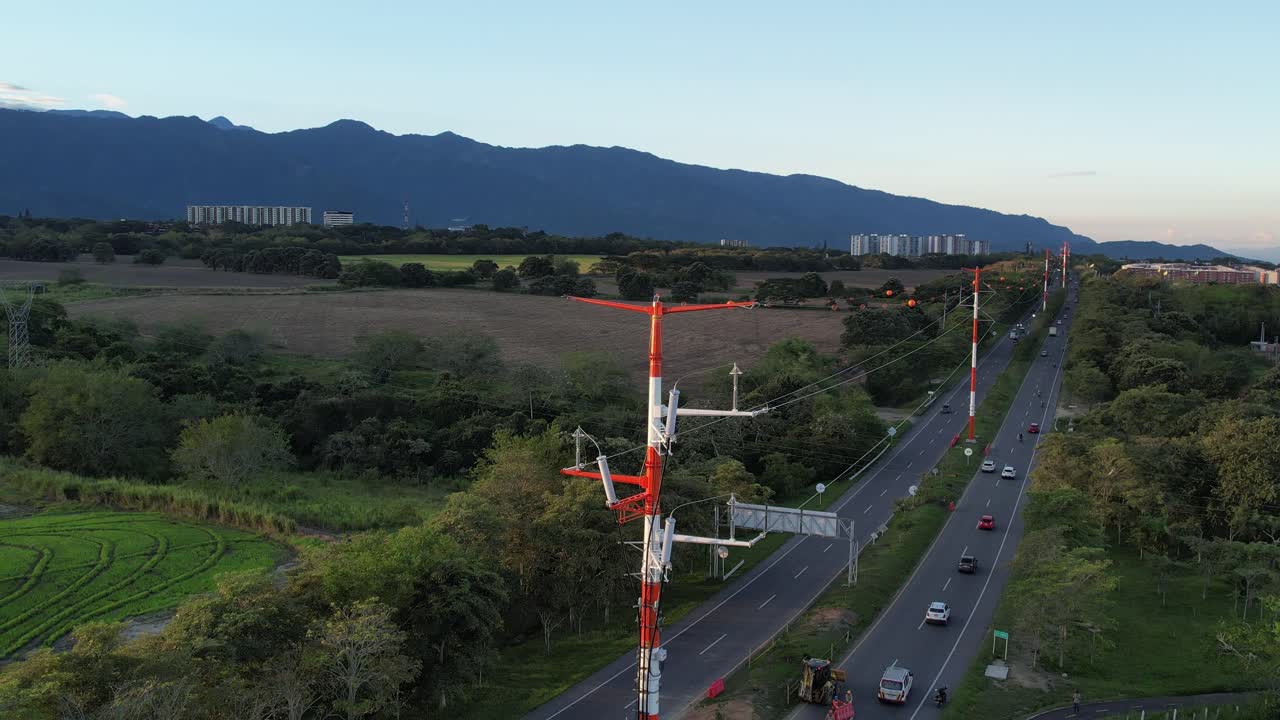 Zoom out drone shot of an electricity transmission tower with a highway and farmland stretching on both sides