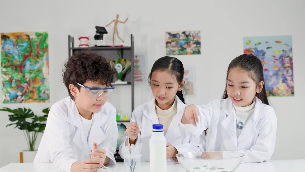 白衣とゴーグルを着用した3人の若いアジア人学生が、授業中に化学実験を行っている。
