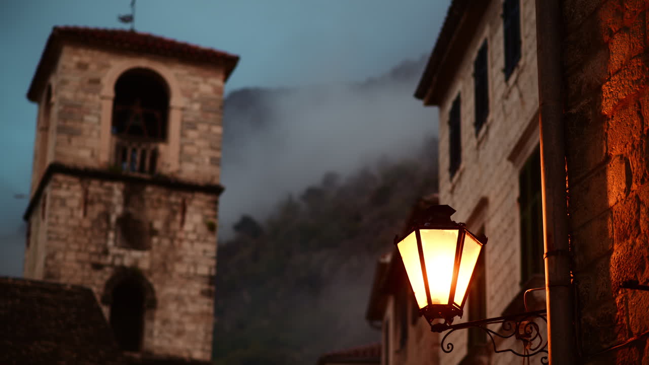 Vecchi edifici in pietra e un lampione illuminato creano una scena crepuscolare suggestiva. Centro Storico di Cattaro, Montenegro