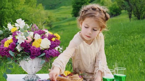 a little girl in a smart dress sits on a table decorated with flowers and eats a chocolate finge