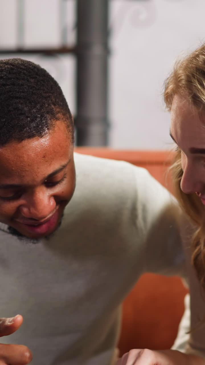 Cheerful white lady shares sweet memories about family with African-American boyfriend looking at pictures on couch in living room slow motion
