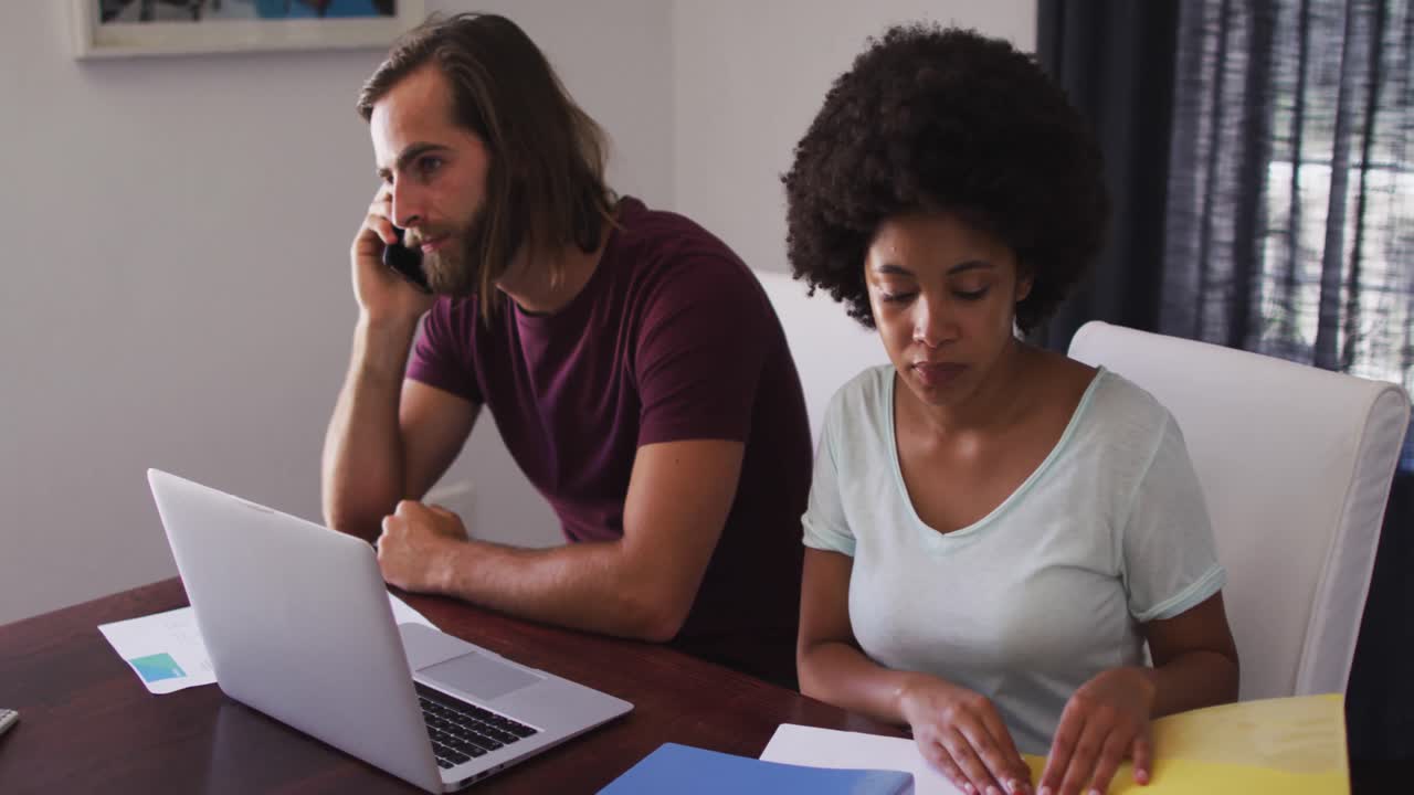 Mixed race couple calculating finances and talking on smartphone at home