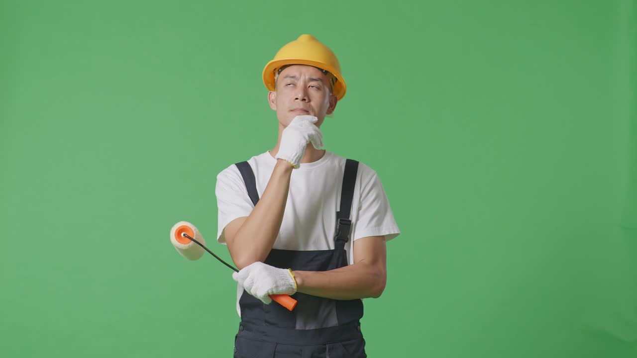 Asian Man Painter Wearing Safety Helmet Thinking And Looking Around Then Raising His Index Finger While Standing In The Green Screen Background Studio