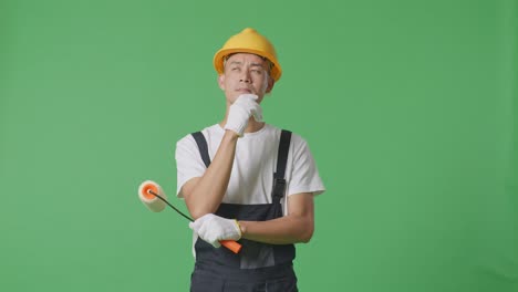 asian man painter wearing safety helmet thinking and looking around then raising his index finger while standing in the green screen background studio