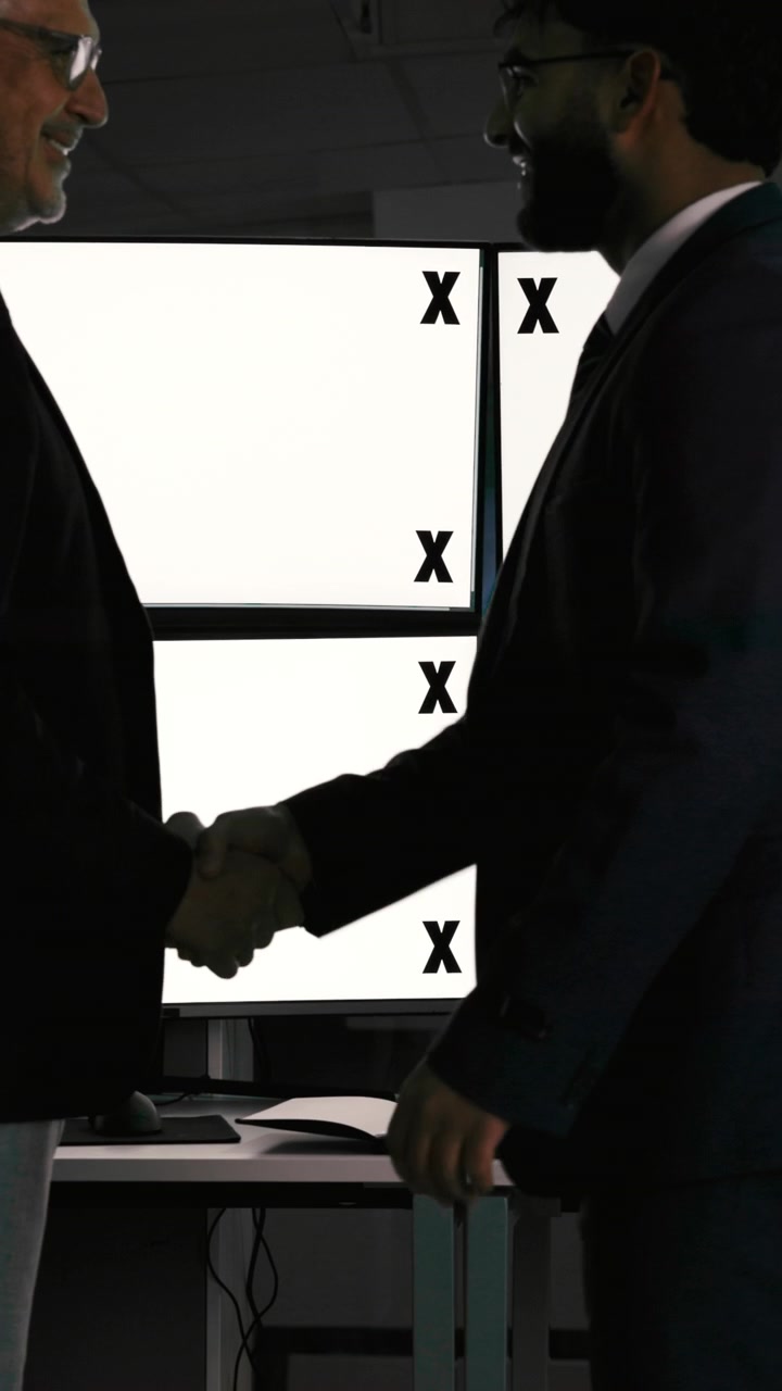 Due uomini d'affari che si stringono la mano in un ufficio buio