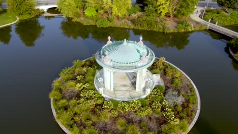 Cenador---Estructura-Arquitectónica-De-Sombra-Redonda-En-Un-Hermoso-Entorno-Fluvial,-Dron-Aéreo-Que-Se-Eleva-Inclinado-Hacia-Abajo