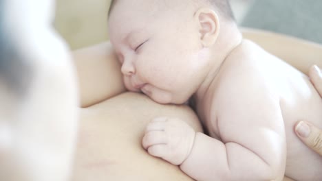 Fussy-newborn-baby-gets-breastfed-before-falling-asleep-in-mother's-arms-as-she-strokes-and-caresses-his-back-while-doing-skin-to-skin