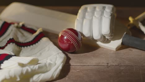 Cricket-Still-Life-With-Close-Up-Of-Bat-Gloves-Stumps-Jumper-And-Bails-With-Ball-Rolling-Into-Frame