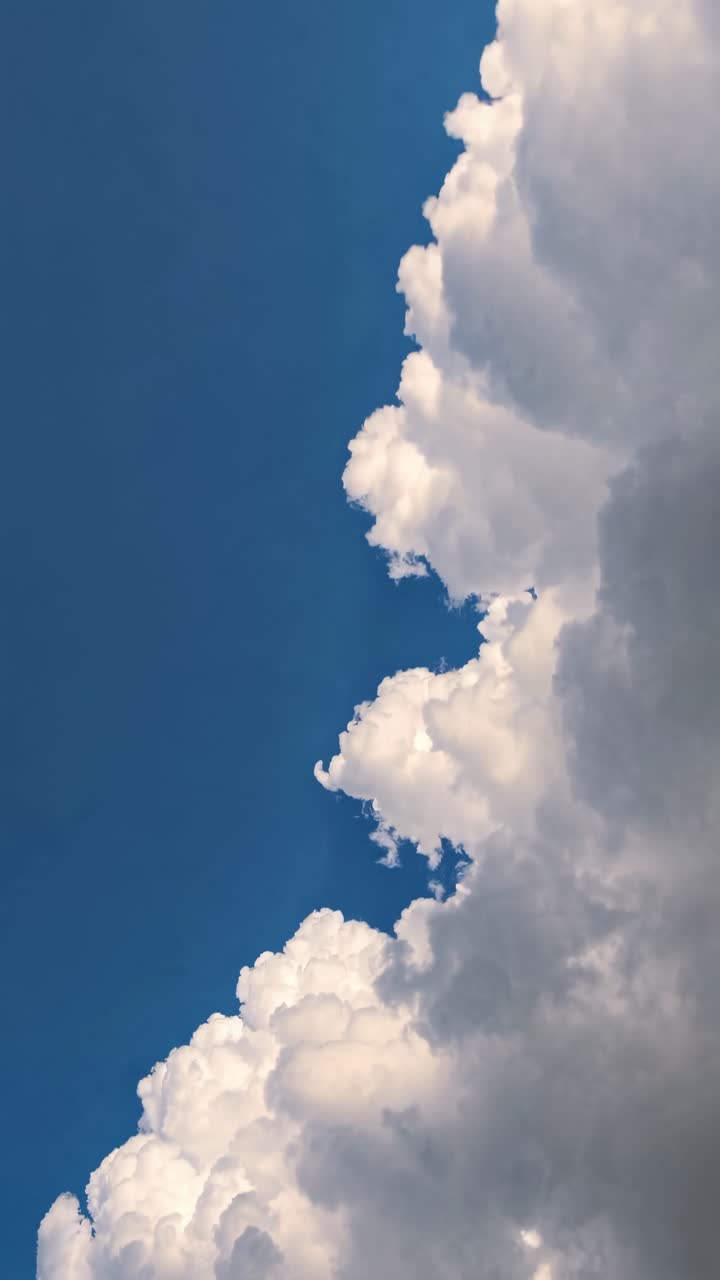 A video captures fluffy white clouds against a deep blue sky from a low-angle perspective
