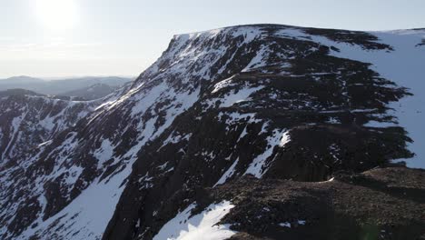 aerial drone footage rising above steep mountain cliffs and snow filled gullies near ben macdui in the cairngorms national park, scotland as sunshine reflects off of a snow covered winter ridge