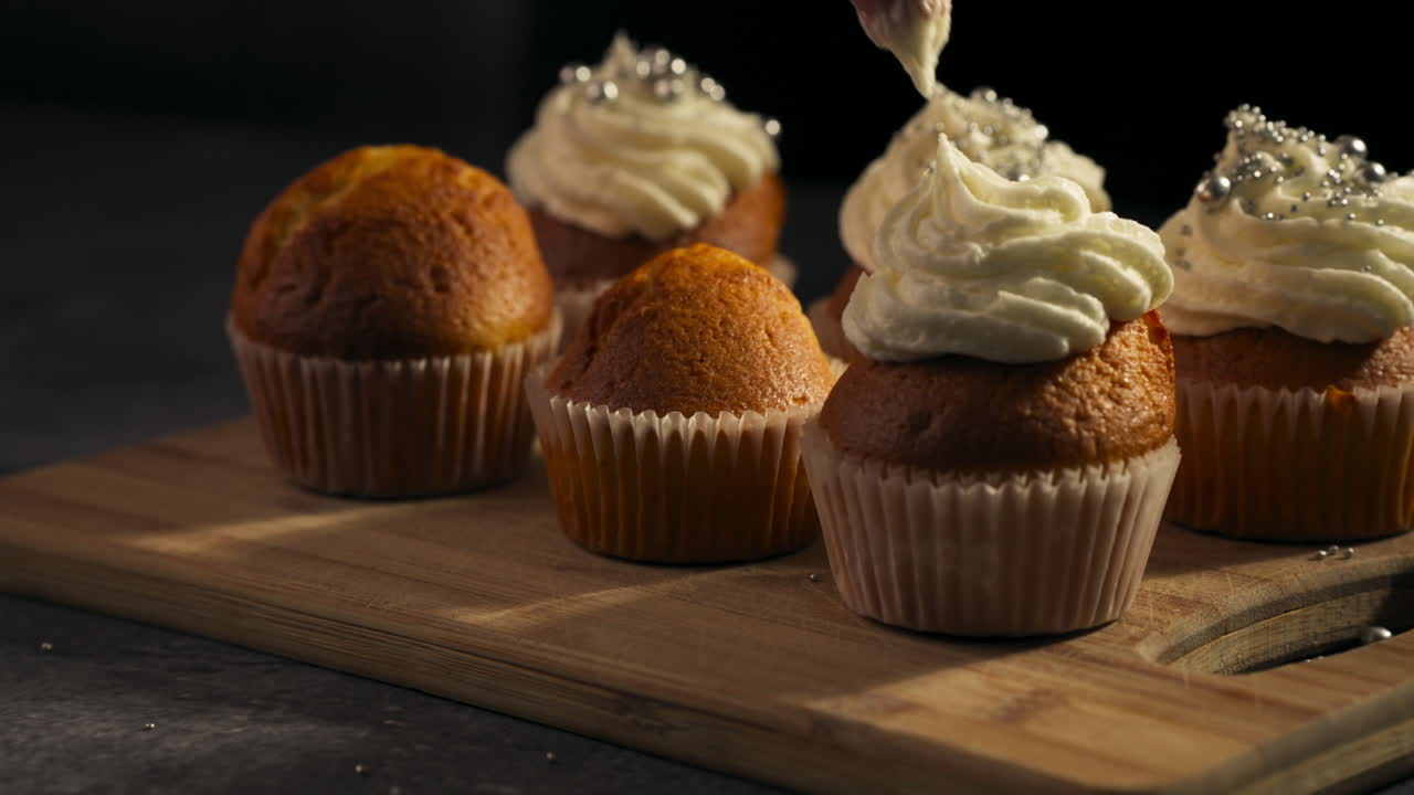 Cupcakes with whipped frosting ready for a dessert showcase presentation, tracking right slow motion as frosting pipes on in swirl
