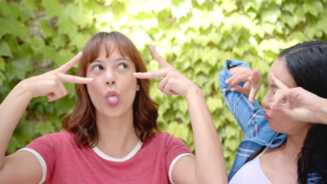 Two-young-biracial-female-friends-are-making-playful-gestures-with-their-hands-near-their-eyes