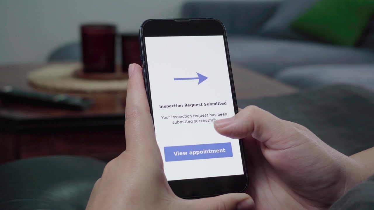Mani tengono un telefono che mostra una conferma di 'Richiesta di Ispezione Inviata' con una call-to-action blu 'Visualizza appuntamento'