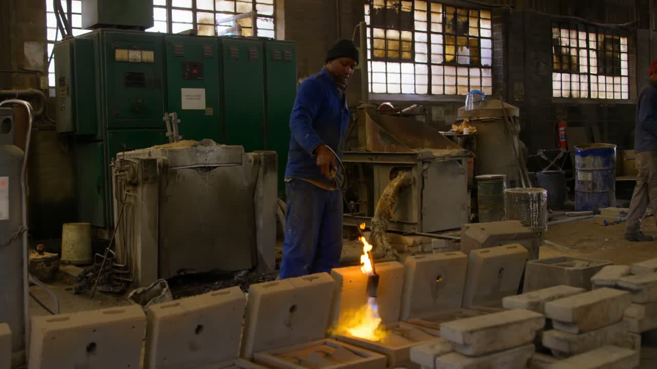 Lavoratore che riscalda uno stampo metallico con un cannello in un'officina di fonderia 4K