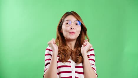 Cheerful-young-Asian-woman-with-eyeglasses-raising-hands-up,-shaking-and-having-fist-pump-from-happiness,-smiling-woman-face,-green-screen-background