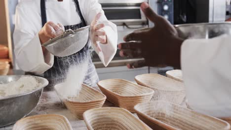 Diverse-bakers-working-in-bakery-kitchen,-pouring-flour-on-baskets-in-slow-motion