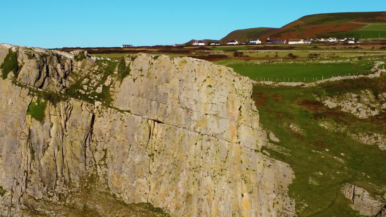 Aerial Orbiting Steep Clifface with Fields Behind with Rhossili Village in Background. Tourist Destination in South Wales UK. Travel Nature Drone Clip. Beautiful Welsh Gower Peninsula Coast