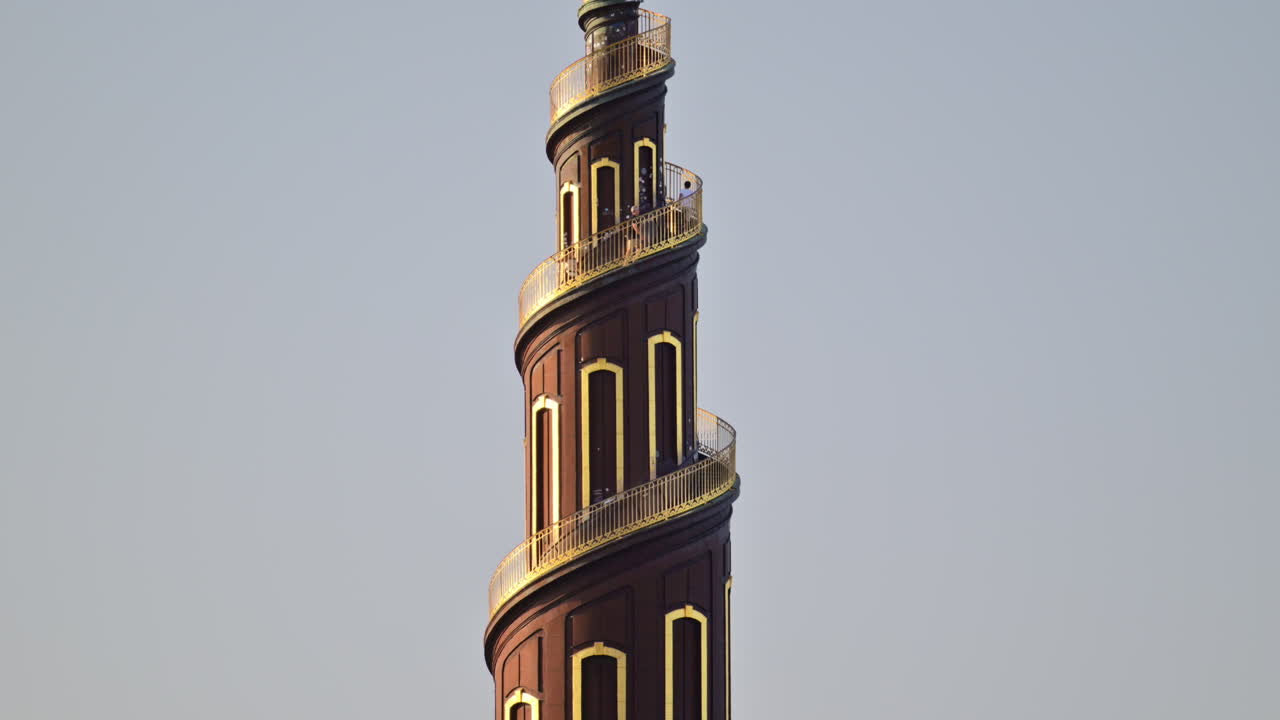 Guglia barocca della Chiesa del Nostro Salvatore che si erge sopra gli alberi verdi, con un cielo limpido sullo sfondo. Copenhagen, Danimarca