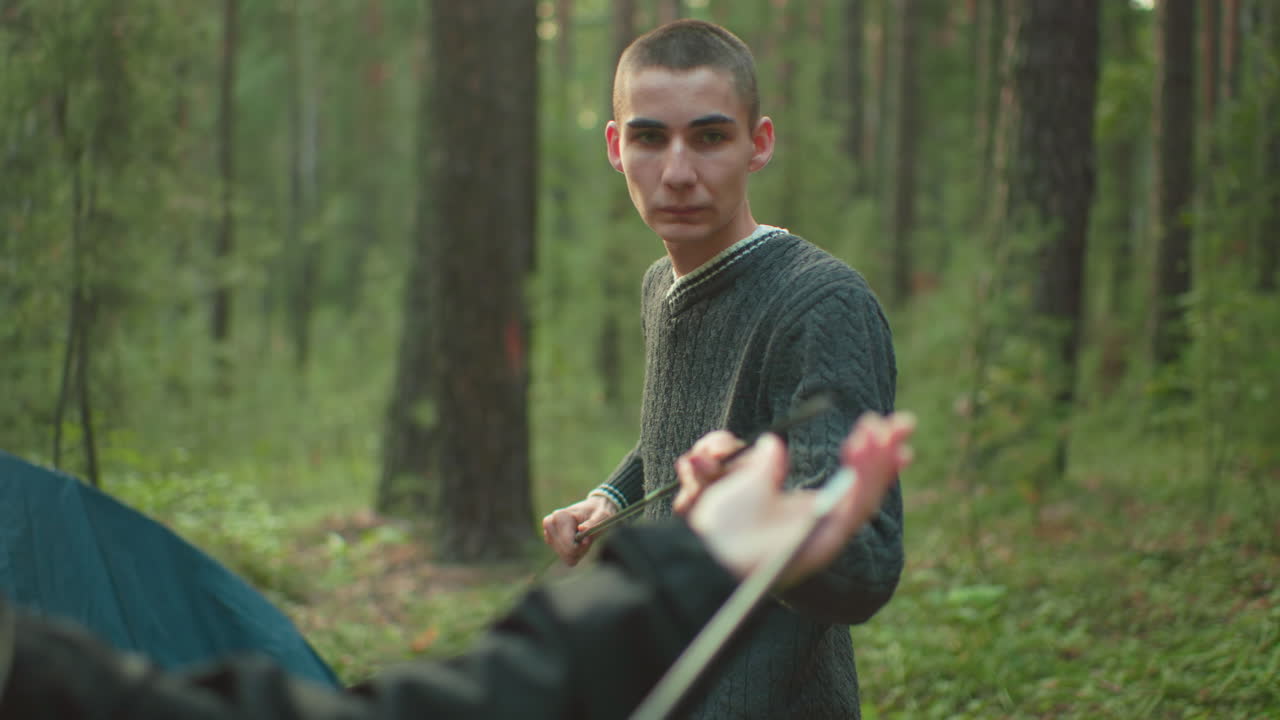 Duo lovers standing in wooded forest environment fixing flexible tent pole together while preparing campsite, surrounded by green foliage and tall trees, engaging in teamwork