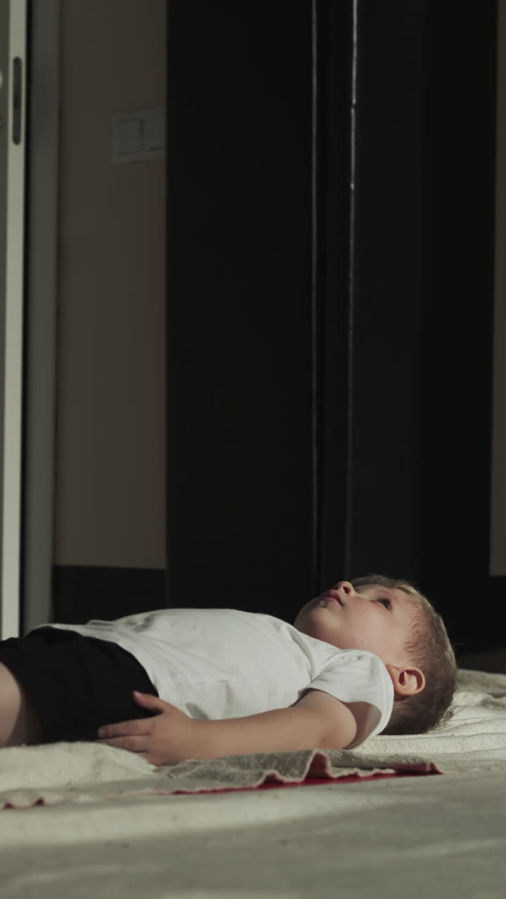 아이는 스포츠 센터에서 싱 봉투 근처에 휴식을 취합니다. 어린 소년은 어린이 체육관에서 무술 연습을 한 후 느린 동작으로 누워 있습니다. 유아는 바닥 개에 긴장을 풀고 있습니다.