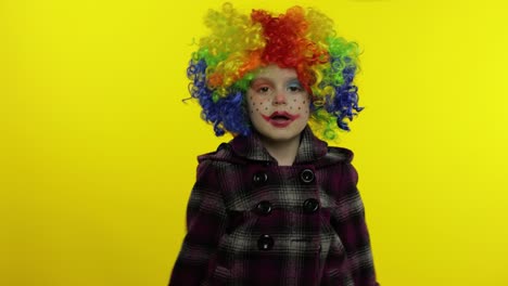una niña payasa con una peluca colorida haciendo caras tontas. divirtiéndose, mostrando trucos. halloween