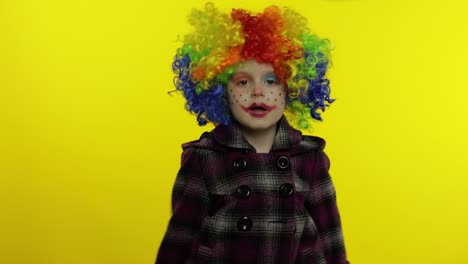 little child girl clown in colorful wig making silly faces. having fun, shows tricks. halloween