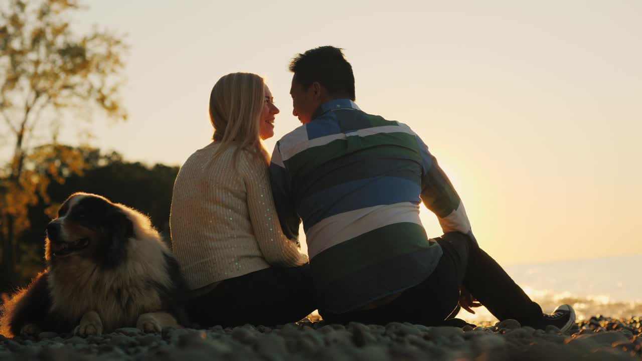 젊은 부부는 개 근처의 해변에서 휴식을 취하고 있습니다.