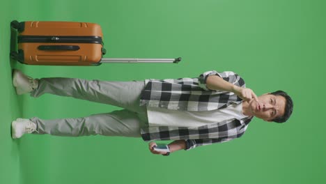 full body of asian male traveler with luggage and passport looking at camera and shouting at someone while standing in the green screen background studio