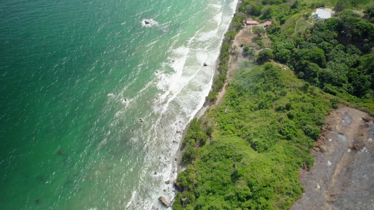 Long aerial view over the coastline, showing waves, trees, and distant mountains in Venezuela