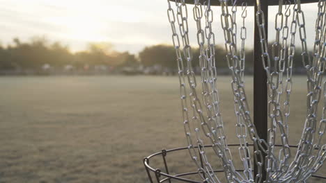 white frisbee goes into disc golf basket and is retrieved by man during sunset on disc golf course | disc golf