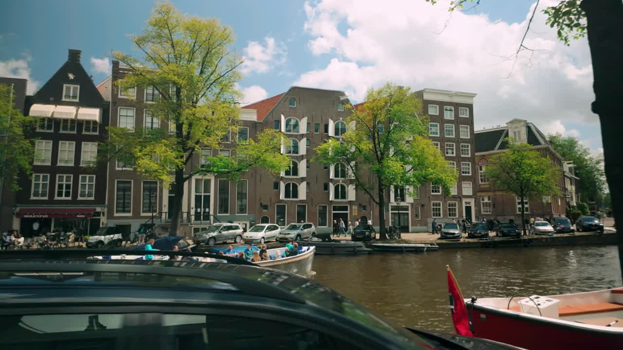 A Boat Navigating an Amsterdam Canal Lined with Historic Buildings