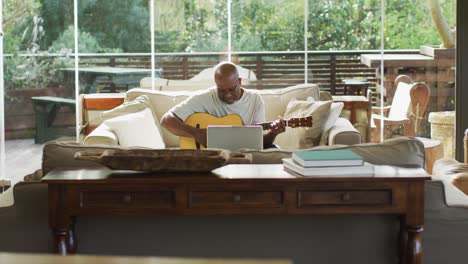 feliz hombre mayor afroamericano en la sala de estar tocando la guitarra acústica y usando computadora portátil