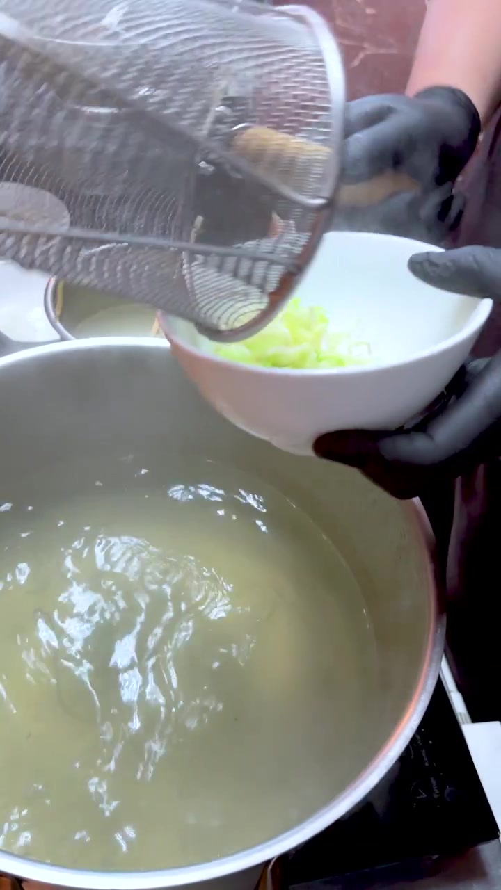 Un venditore di cibo da strada bolle i noodles in un colino a rete prima di servirli in una ciotola.