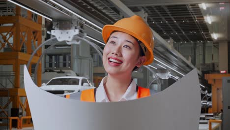 close up de ingeniera femenina asiática con casco de seguridad mirando el plano en sus manos y mirando a su alrededor mientras estaba de pie en la fábrica de automóviles ev