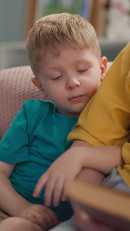 attentive grandson listens to granny reading fairy tale book sitting on sofa closeup slow motion. toddler boy stunned by magic story. family relationship