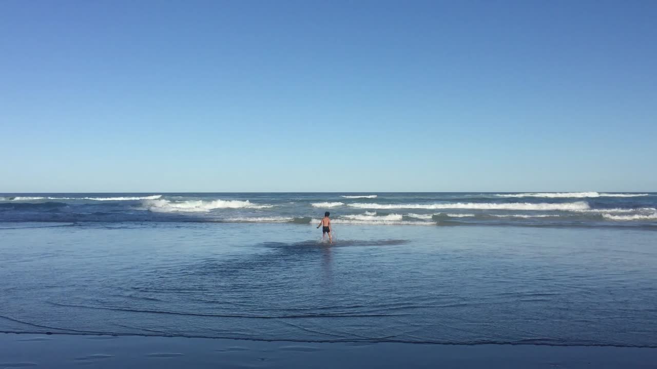 Tranquil day with a little boy running on the sea water against beautiful cloudless blue sky, summer paradise.