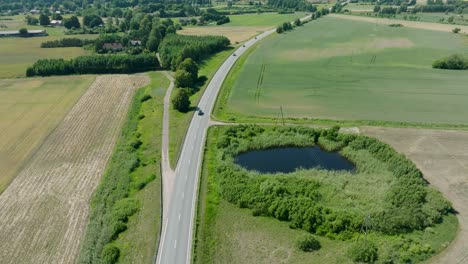 aerial establishing shot of a rural landscape, countryside road with trucks and cars moving, lush green agricultural crop fields, sunny summer day, wide drone shot moving forward, tilt down