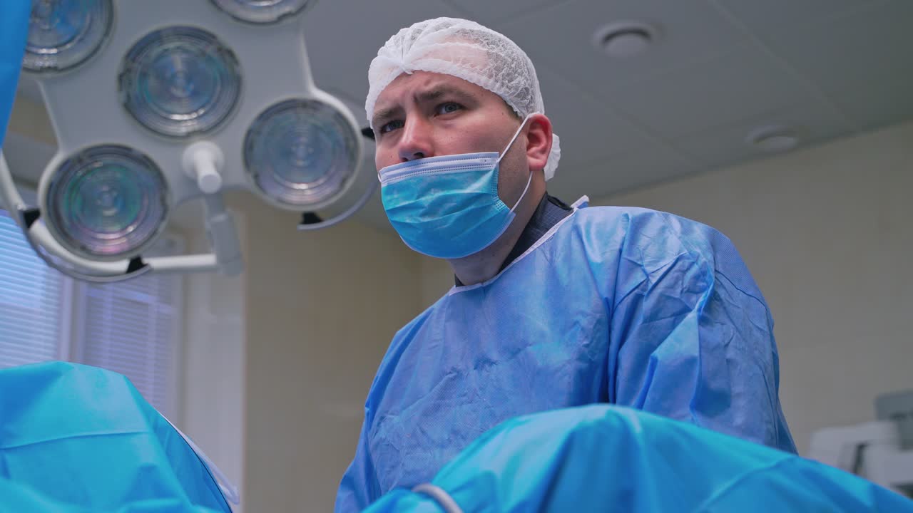 Portrait of a surgeon looking seriously. Medical specialist in a uniform and mask during the complicated surgery in modern operating room.