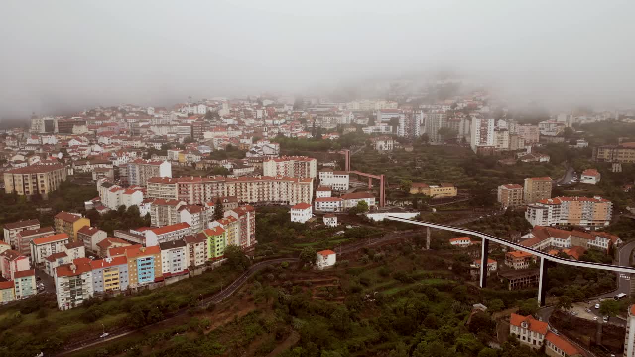 A bird's-eye perspective of Covilha Village showcases a tall skyscraper, a suspended bridge, and narrow streets - 2