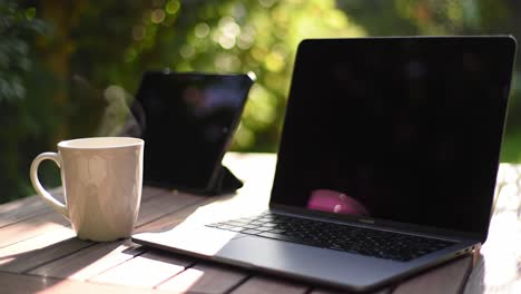 a tranquil outdoor workspace featuring a laptop, tablet, and hot beverage, perfect for productive moments in nature's embrace